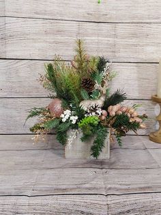 a vase filled with flowers and greenery next to a candle on a wooden table