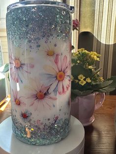 a vase with flowers painted on it sitting on a table next to a potted plant