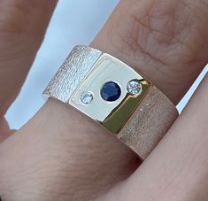 Natural Sapphire (3mm) and diamond (2mm - 0.03 carats each) sterling Silver and 14k Gold Ring, Wide Band Silver ring Wide: 10mm Thickness: 1,5mm Dark Blue natural sapphire : 3mm (0.10ct) Natural diamond: 2mm each ( 0.03carats) This natural Sapphire and diamonds Ring in Solid 925 Sterling Silver and 14k Gold is absolutely beautiful. Handcrafted Ring. Ring will be packed in a beautiful gift box and bag with Pearls Box logo ready for giving! PLEASE NOTE- shipping time does not include making time. Wide Rings With Stones, Wide Band Engagement Ring Unique, Wide Band Diamond Rings, Wide Band Engagement Ring, Thick Gold Ring, Wide Gold Ring, Mens Ring Designs, Blue Sapphire Diamond Ring, Silver Gold Jewelry