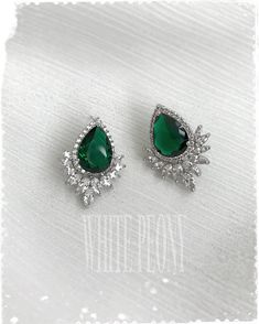 pair of earrings with green stone and crystal stones on white fabric background, close up