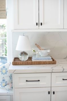 a white kitchen with marble counter tops and cabinets in the corner, along with a lamp