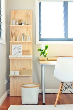 a wooden shelf sitting next to a white chair in a living room under a window