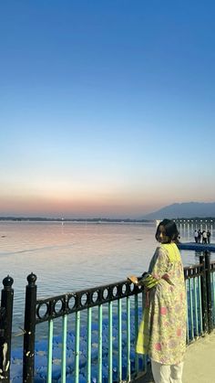 a woman standing next to a metal fence near the water