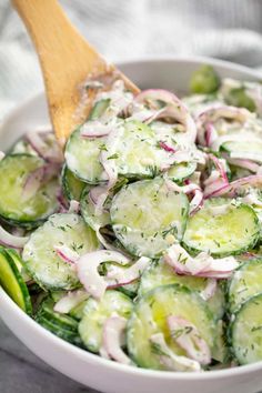 cucumber and onion salad in a white bowl with a wooden spoon on the side