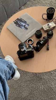 a coffee table topped with lots of different types of cameras and electronics on top of it