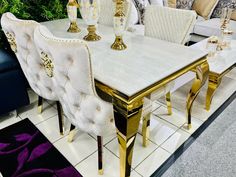 a dining table with white chairs and gold trimmings in a room filled with couches