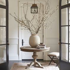 a vase with flowers on top of a table in front of an open door and two chairs