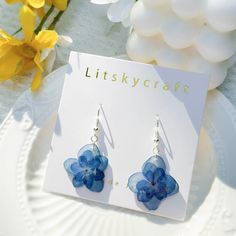 a pair of blue flower earrings sitting on top of a white plate next to yellow flowers