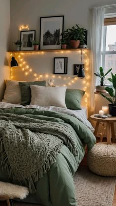 a bed with green comforter and lights on the headboard, in front of a window