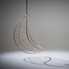 a metal object hanging from a wire on a gray background with shadows in the foreground