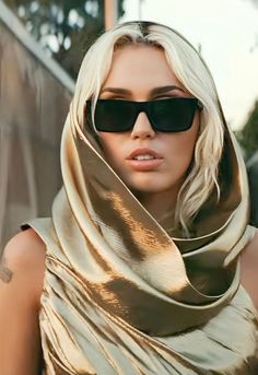 a woman wearing sunglasses and a gold dress with a scarf around her neck is looking at the camera