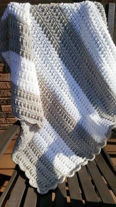 a white crocheted blanket sitting on top of a wooden bench next to a brick wall