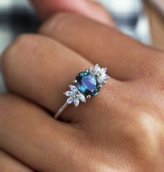 a woman's hand holding a ring with blue stones and leaves on the band