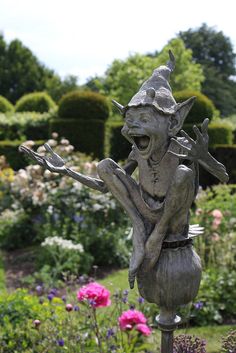 a statue of a troll sitting on top of a metal pole in a flower garden