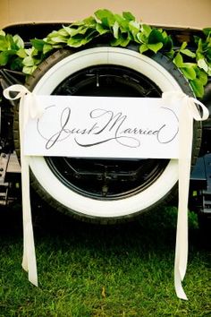 a sign that says just married sitting on the back of a truck with greenery around it