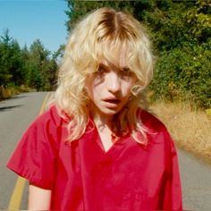 a blonde haired woman in a red shirt is standing on the side of a road