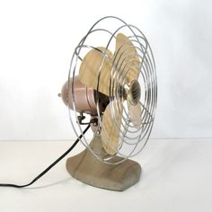 an old style desk fan sitting on top of a wooden base with a cord attached to it