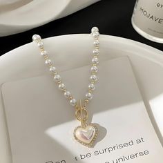 Drape yourself in elegance with this Coquette Heart Pearl Necklace. Lustrous pearls meet a charming heart pendant, creating a timeless piece that adds a romantic glow to any ensemble. Perfect for those seeking a blend of classic grace and endearing charm. Coquette aesthetic Heart shaped pearl with rhinestone pendant Pearl beaded design Zinc alloy Coquette Pearl Necklace, Heart-shaped Pearl Necklace For Party, Valentine's Day Pearl Necklace For Party, Party Jewelry With Pearl And Heart Charm, Elegant White Heart Pendant Necklace, Valentine's Day Pearl Jewelry With Pearl Chain, Elegant White Heart Necklace, Heart Shaped Pearl Charm Necklace For Party, Heart-shaped Pearl Charm Necklace For Party