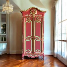 a pink and gold painted armoire in a room with wood floors, chandelier and windows