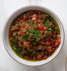 a white bowl filled with lots of food on top of a marble counter next to a spoon