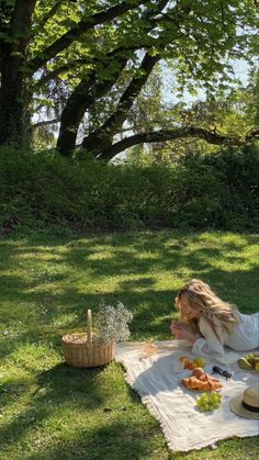 a woman sitting on top of a grass covered field next to a basket of fruit