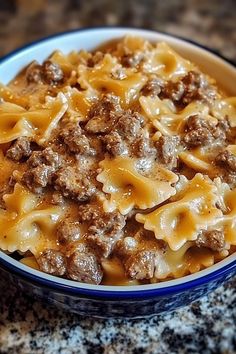 a close up of a bowl of food with meat and noodles in it on a table