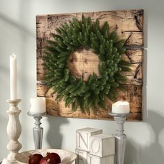 a christmas wreath is hung on the wall above a bowl of fruit and two candles