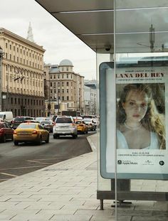 a bus stop with cars parked in front of it and a movie poster on the side