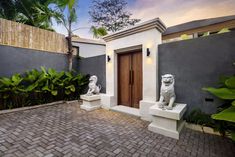 two white statues sitting in front of a door on top of a brick floored courtyard