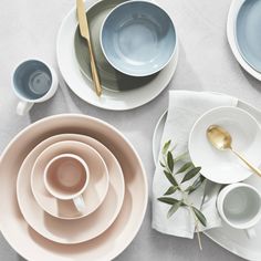 plates, cups and spoons are arranged on a white tablecloth with goldware