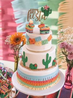 a three tiered cake with cactus decorations on top and flowers in vases next to it