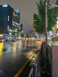 a city street at night with cars and buses driving on the road in the rain