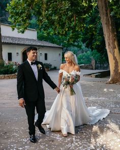 a bride and groom holding hands walking down the street