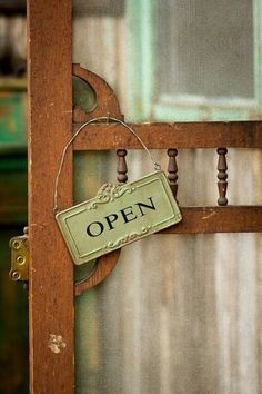 an open sign hanging from the side of a wooden door with metal bars and wood posts