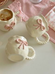 two mugs with pink bows on them sitting next to a napkin and some other items