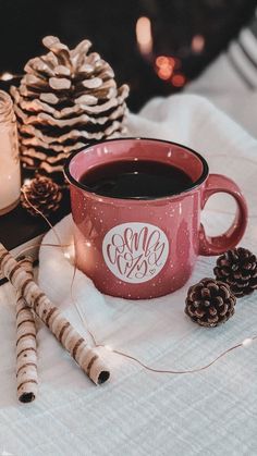 a cup of coffee sitting on top of a table next to pine cones and candles