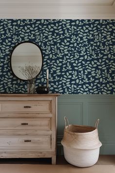 a dresser and mirror in a room with blue leaves on the wall, along with a white basket