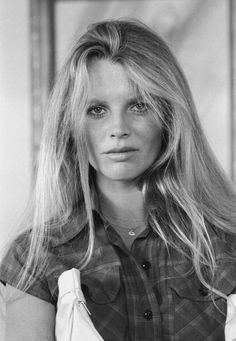 a black and white photo of a woman with long hair wearing an apron looking at the camera