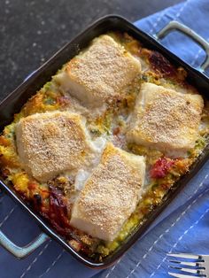 a casserole dish with meat and vegetables in it on a blue towel next to a fork