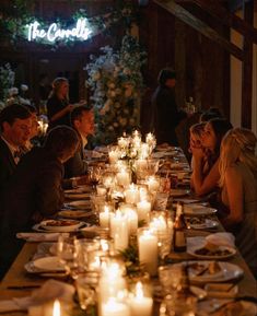 a group of people sitting around a dinner table with lit candles on the dining room table