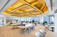 an office with people working on their laptops in the middle of tables and chairs