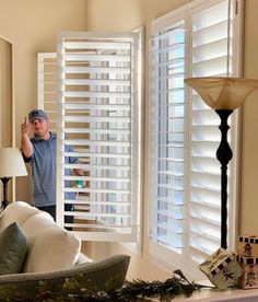 a man standing in front of a living room window with shutters open and blinds closed