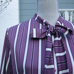 "1980s secretary blouse with a tie neck and varying width lilac purple, mulberry & white vertical stripes vertical. Women's size large blouse, Graff Californiawear. The blouse has sleeves that cuff at the wrist with a button. The 5 buttons down the front and each at on the cuffs are a purple plastic. The tie is built in, an extension of the collar. The tie is 1.5\" wide or 3.8 cm and flares out to over 2\" at each end. It is 24\" long or cm long on each side from the collar to the tip. The f Patterned Blouse Outfit, Purple Fitted Collared Blouse, Classic Collared Purple Blouse, Classic Purple Collared Blouse, Purple Button-up Blouse For Work, Purple Button-up Blouse For Party, Black Party Tops, Purple Fitted Button-up Blouse, Secretary Blouse