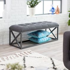 a grey bench with two pillows on it in front of a white brick wall and potted plant