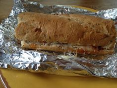 a sandwich is wrapped in aluminum foil on a yellow plate