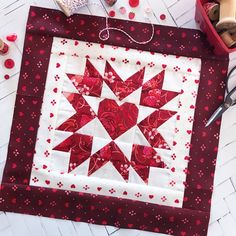 a red and white quilted table topper with scissors, thread and spools