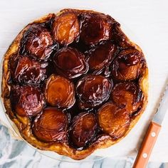 a pie sitting on top of a white plate next to a knife and orange handled utensil