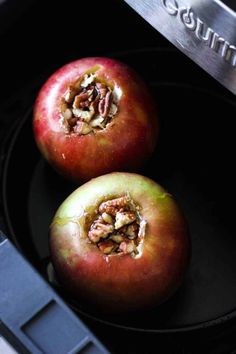 two apples sitting on top of a black plate next to a toaster oven door