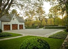 a house with a driveway and two garages in the middle of it, surrounded by greenery