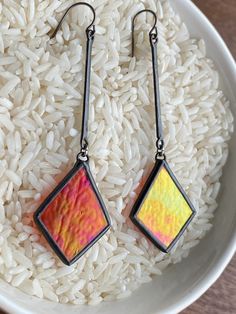 a pair of earrings sitting on top of white rice in a bowl with silver ear wires